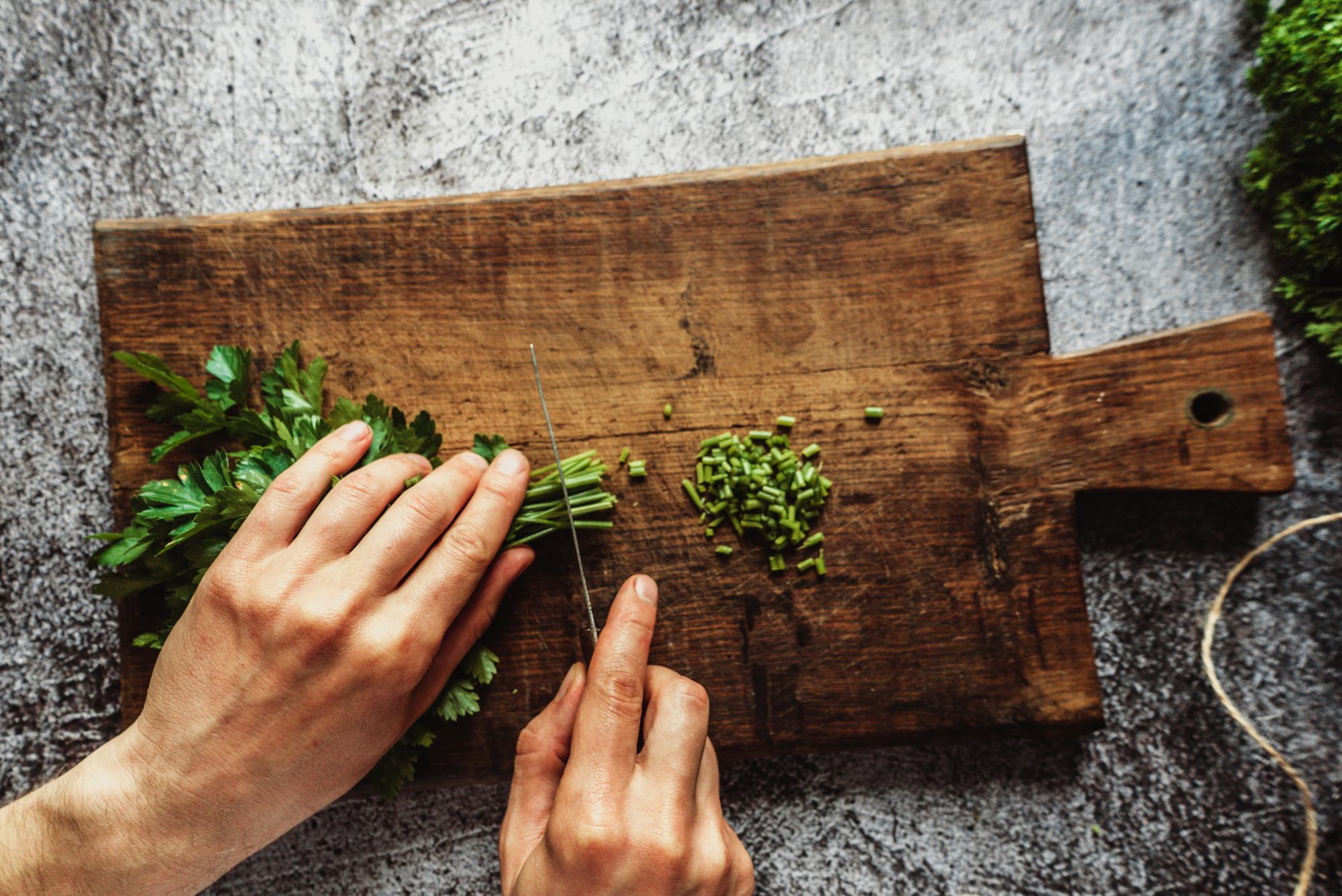 Close-up: hands slicing herbs on wooden board
